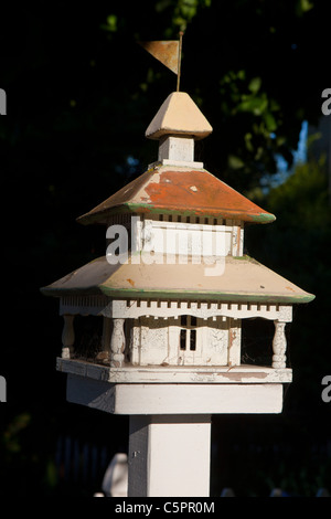 White bird house with metal roof and flag on top near sidewalk. Stock Photo