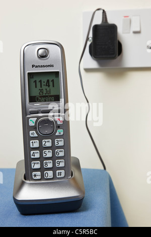 Panasonic cordless digital telephone handset charging on a phone charger base unit plugged into a wall socket. England UK Britain Stock Photo