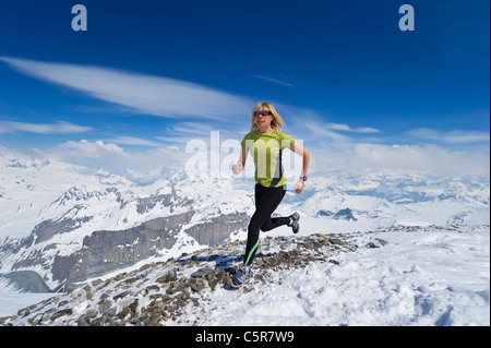 Woman jogging across snowy mountains. Stock Photo