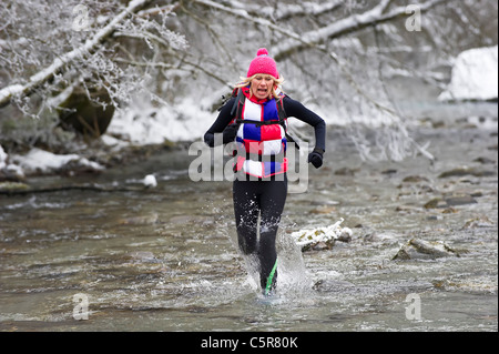 A jogger running through a snowy river bed and it's cold alpine waters. Stock Photo