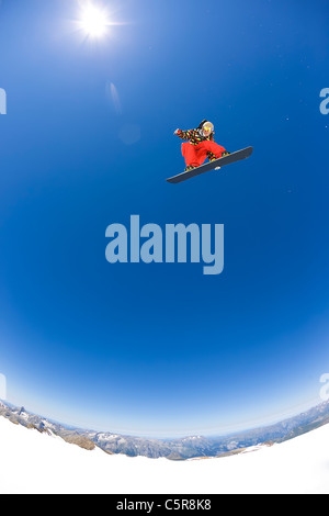 A Snowboarder flying high above the mountains and glaciers in the sun.