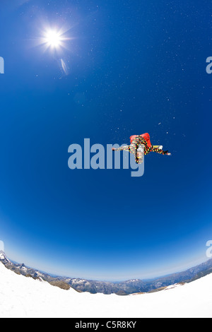 Snowboarder back flipping over glacier. Stock Photo