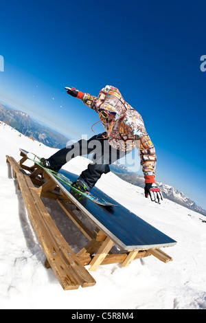 A snowboarder slides a picnic table on a mountainside Stock Photo