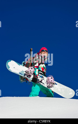 A snowboarder looks out over the snowy mountains and smiles. Stock Photo