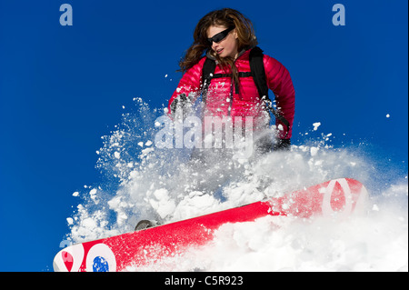 A female snowboarder riding hard through fresh powder snow. Stock Photo