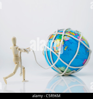 A wooden figurine pulling a globe rolled up by rope Stock Photo