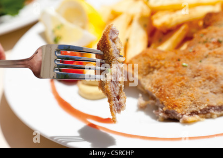 Close up of Viennese Schnitzel with french fried potatoes with piece of meat on fork Stock Photo