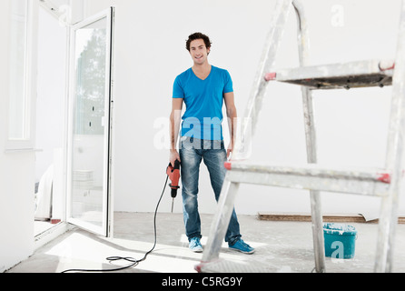 Germany, Cologne, Young man holding electric drill in renovating apartment Stock Photo