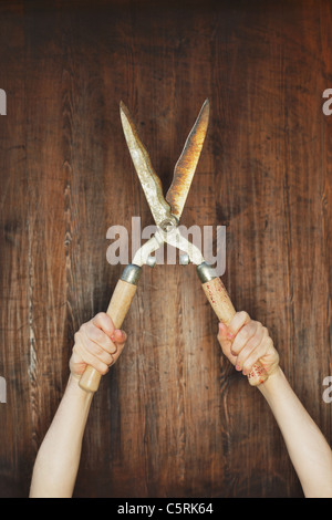Man holding old manual hedge trimmer in front of wooden background. Stock Photo