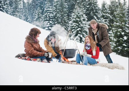 Austria, Salzburg Country, Flachau, Young men and women sitting near fireplace and making tea in snow Stock Photo