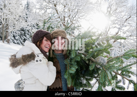Austria, Salzburg Country, Flachau, Young man and woman carrying christmas tree in snow