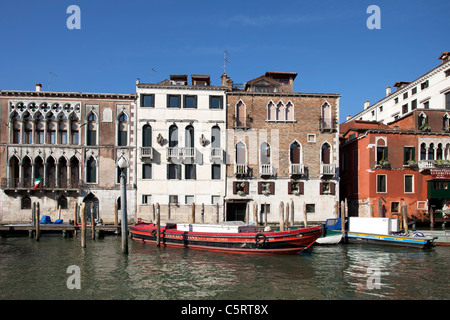 Venice, the Grand Canal between old historic buildings.  Flowers on window sills. Red boat parked out front. Stock Photo