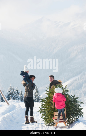 Austria, Salzburg Country, Flachau, View of family carrying christmas tree and sledge in snow Stock Photo