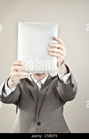 Close up of businessman holding Tablet PC in front of his face against grey background Stock Photo
