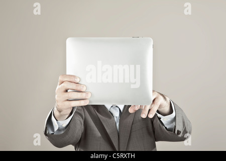Close up of businessman holding ipad in front of his face against grey background Stock Photo