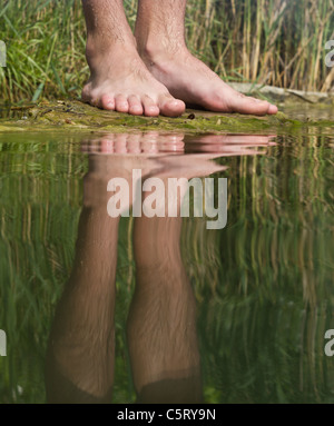 Austria, Vienna, Reflection of man's feet on lakeshore, close up Stock Photo