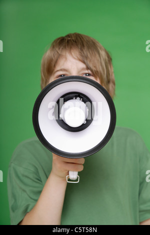 Close up of boy screaming in megaphone against green background Stock Photo