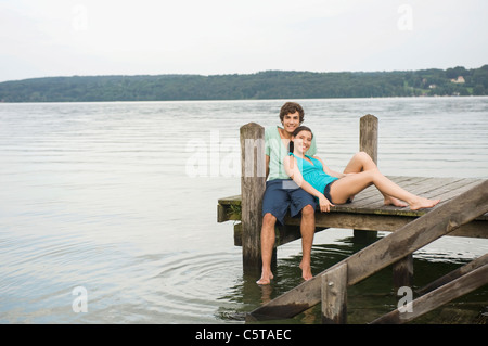Germany, Bavaria, Starnberger See, Young couple sitting on jetty Stock Photo