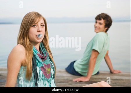 Germany, Bavaria, Starnberger See, Couple on jetty, young woman blowing bubblegum, man in background Stock Photo