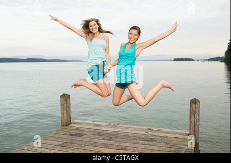 Germany, Bavaria, Starnberger See, Two young women jumping on jetty, laughing, portrait Stock Photo