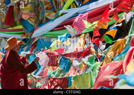Buddhist Monk ties prayer flag to stupa shrine along shores of Qinghai Lake, Qinghai Province, China Stock Photo