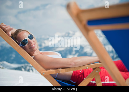 Austria, Salzburger Land, Young woman lying in deck chair, smiling, portrait Stock Photo