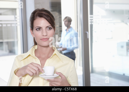 Germany, Cologne, Businesswoman in office taking a coffe break, business man in background Stock Photo