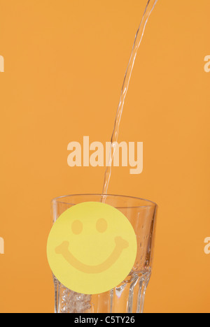 Water being poured into glass, Smiley in foreground Stock Photo