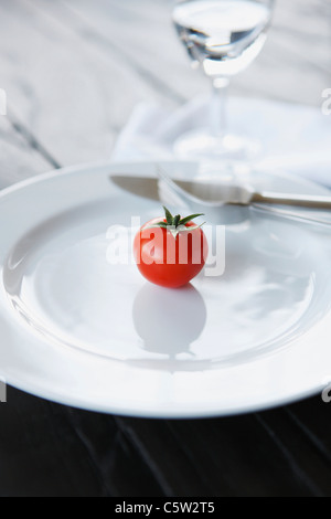 Single Tomato and cutlery on white plate, close-up Stock Photo