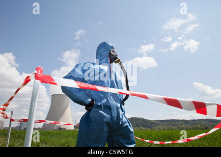 Germany, Bavaria, Unterahrain, Man with protective workwear standing in field at AKW Isar and cordon tape in foreground Stock Photo