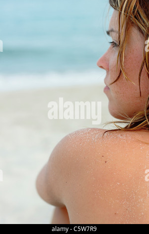 Italy, Sardinia, Young woman sitting on beach, rear view, close-up Stock Photo