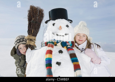 Germany, Bavaria, Munich, Boy (8-9) and girl (8-9) standing next to snowman, portrait Stock Photo