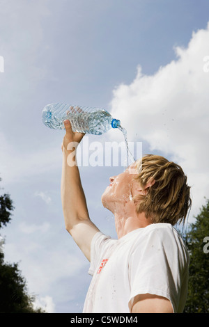 Germany, Berlin, Young man pouring water over face, side view, portrait Stock Photo