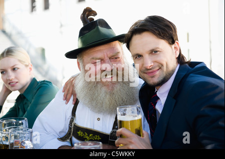 Germany, Bavaria, Upper Bavaria, Man in traditional cosume and businessman in beer garden, smiling, portrait Stock Photo