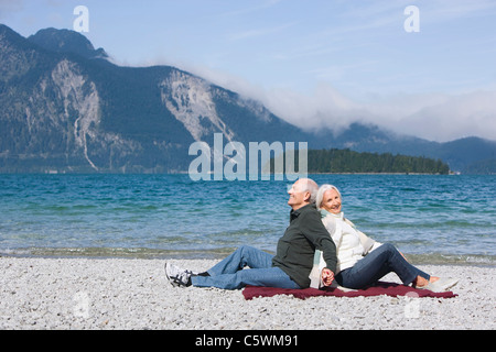 Germany, Bavaria, Senior couple relaxing on lakeshore, sitting back to back Stock Photo