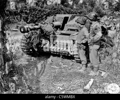 NORMANDY INVASION 1944 Two US soldiers from 3rd Armoured Division with knocked out Sturmgeschutz and dead German crew member Stock Photo