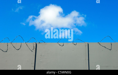 White cloud against blue sky above grey concrete wall and barbed wire Stock Photo