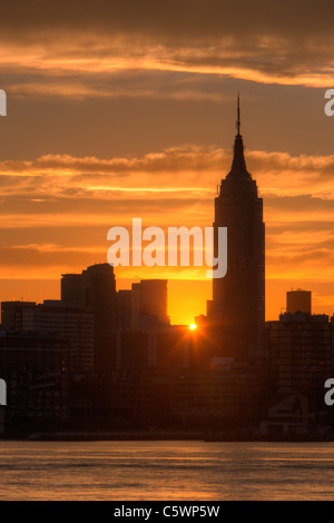 The rising sun shines between Manhattan buildings including the Empire State Building just after sunrise in New York City.