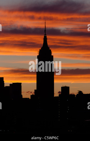 The Empire State Building and other Manhattan buildings are silhouetted against orange colored clouds shortly before sunrise