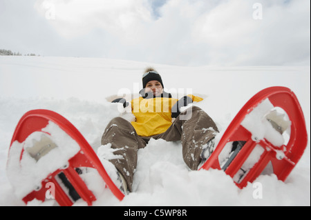 Italy, South Tyrol, Young woman with snowshoes lying in snow