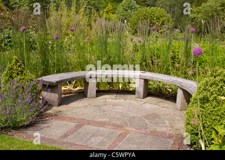 A wooden bench on stone flagstones in a garden in North Yorkshire with purple 'Aliums' growing close by Stock Photo