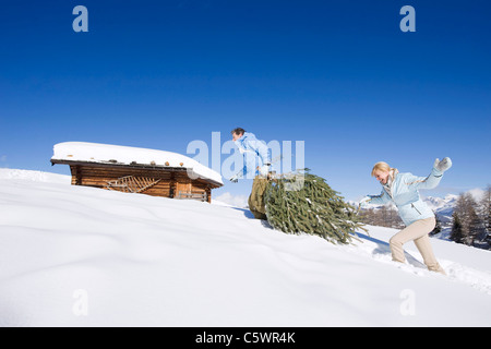 Italy, South Tyrol, Seiseralm, Couple carrying Christmas tree in snow