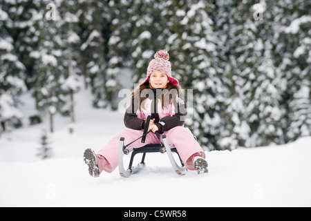 Italy, South Tyrol, Seiseralm, Girl (8-9) sitting on sledge, portrait Stock Photo