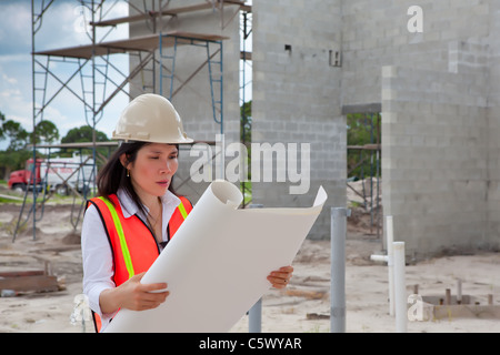Asian Woman Inspector on construction site. Scaffolding, truck, plumbing pipes and block walls in background. Stock Photo