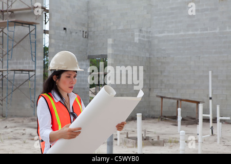 Asian Woman Inspector on construction site. Scaffolding, truck, plumbing pipes and block walls in background. Stock Photo