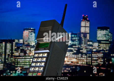 1980’s Mobile Cell Phone MOBIRA CITYMAN 1987 First generation early hand held mobile cell phone Mobira Cityman 1320 launched 1987, with 80’s contemporaneous 1987 London financial city skyline lit at dusk behind including Nat West Tower LONDON CITY Stock Photo