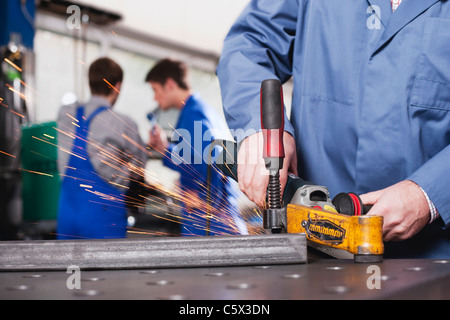 Germany, Neukirch, Person using grinder,  Apprentice and foreman in background Stock Photo