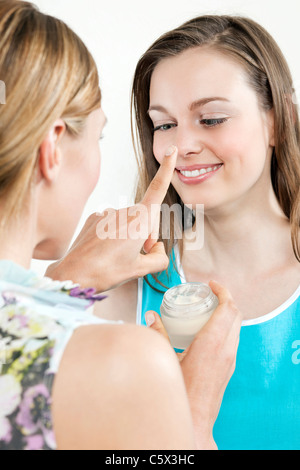 Woman putting cream onto girl friends nose, portrait Stock Photo