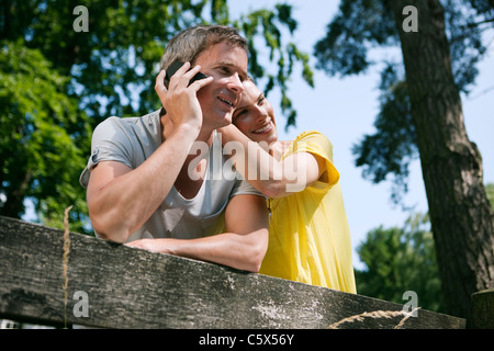 Germany, Hamburg, Couple leaning agianst fence, man using mobile phone Stock Photo