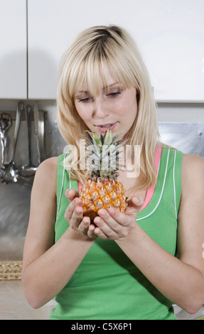 Germany, Berlin, Young woman in kitchen holding pineapple, looking down, portrait Stock Photo